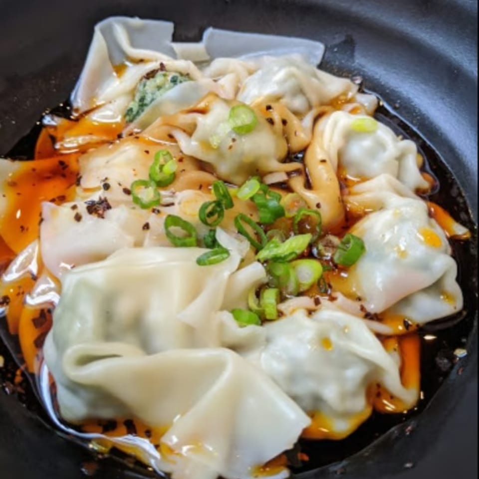 Ginger Asian Kitchen's wontons in chili oil, garnished with chopped green onions.