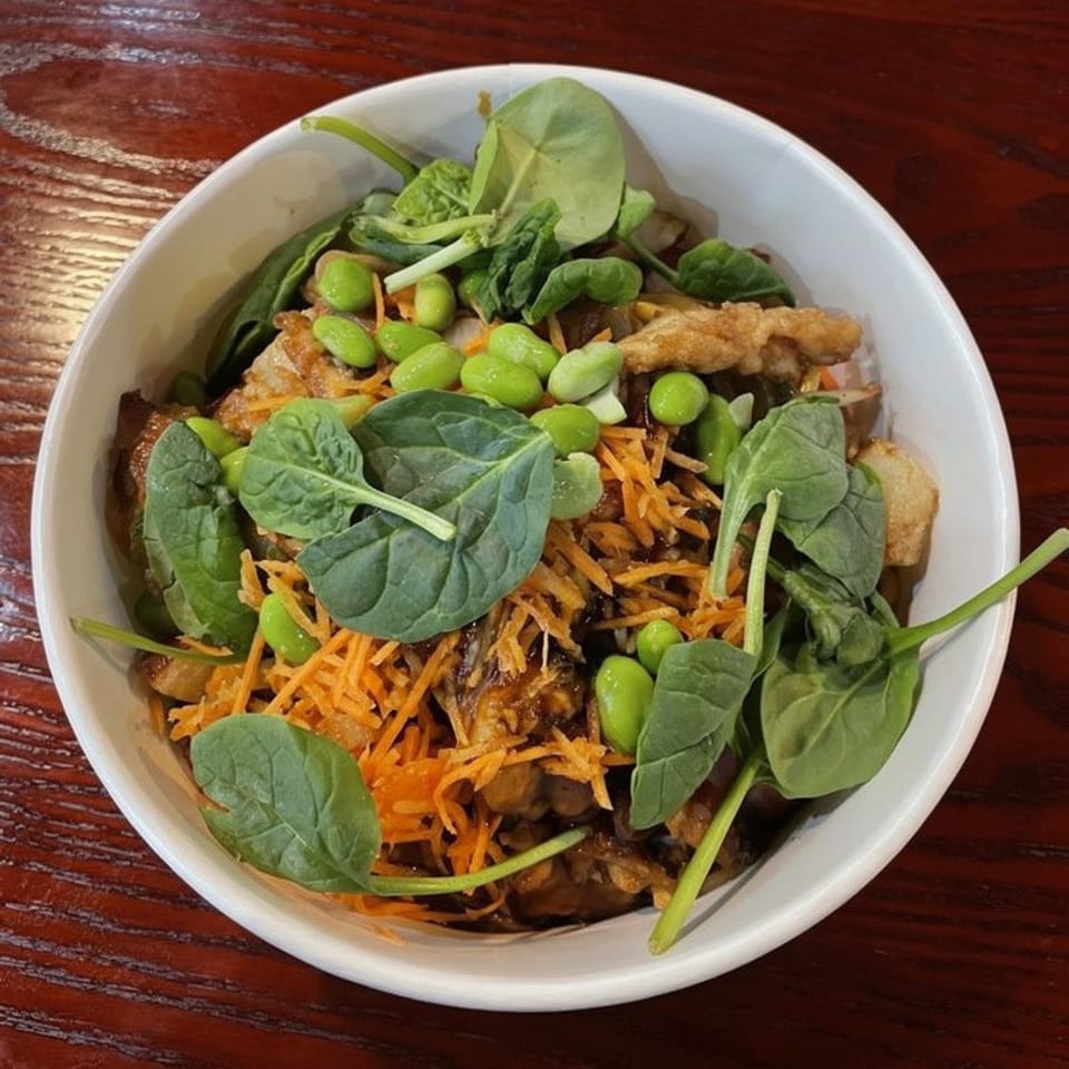 A Ginger Asian Kitchen bowl with chicken, shredded carrots, edamame, and spinach on a wooden table.