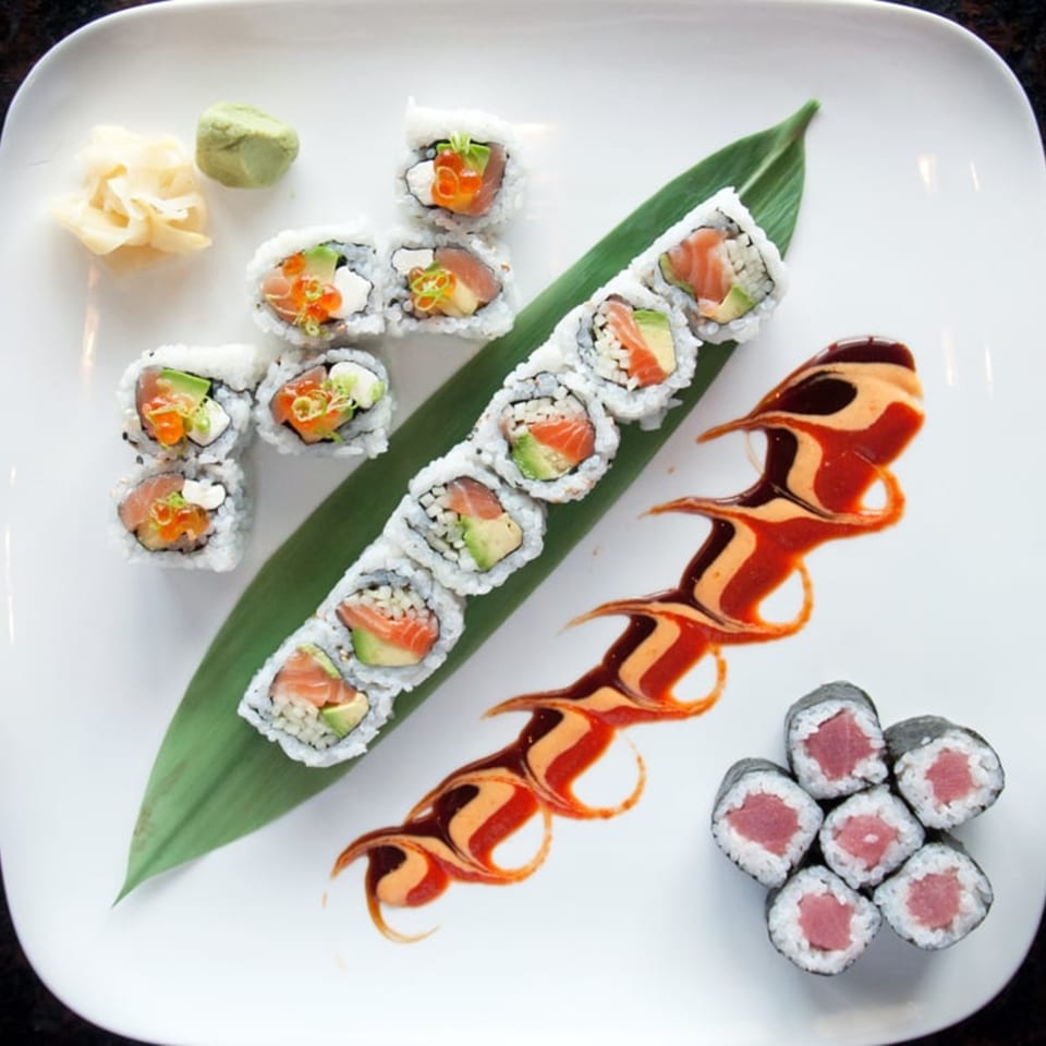 A white plate with various sushi rolls, including salmon, tuna, and avocado, with sauces.